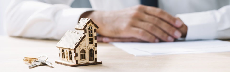 Baufinanzierungsberater Bremen: Mann mit Krawatte erwartet seinen Termin mit kleinem Miniaturhaus auf dem Schreibtisch