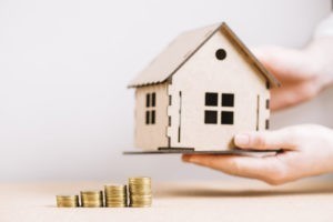 Guenstige Baufinanzierung Bremen: Kleines Holzhaus mit Türmchen aus Geldstücken daneben