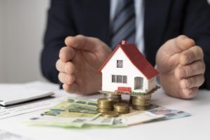 Hausfinanzierung Bremen: Miniaturhaus auf Geld auf deinem Schreibtisch zwischen zwei Handflächen