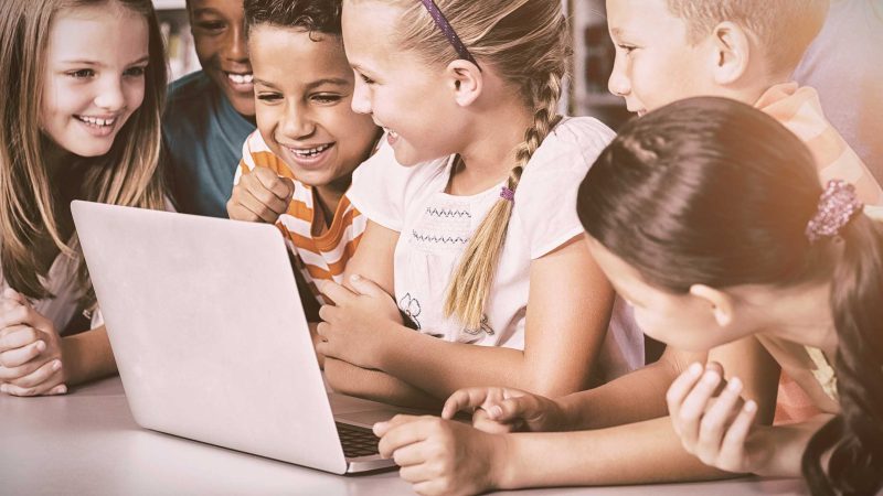 Mehrere Kinder schauen gemeinsam lachend auf einen Laptop