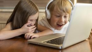 Zwei Kinder schauen gemeinsam auf einen Laptop und lachen