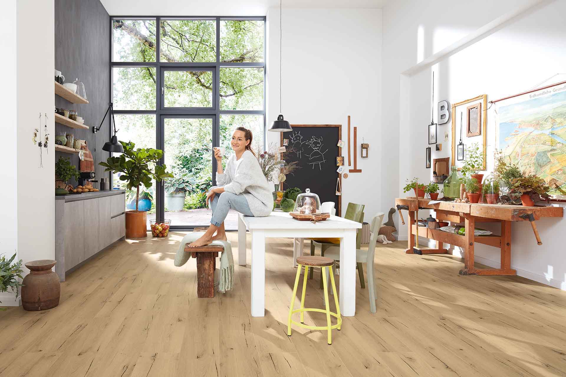 Offene Wohnküche mit großem Fenster, viel Grün und nachhaltigem Bioboden in heller Holzoptik.