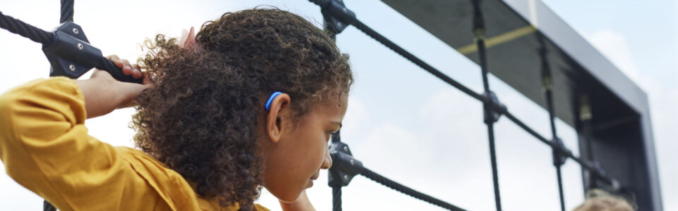 Fröhliches Kind mit Hörgerät auf einem Klettergerüst mit anderen Kindern – Hörgeräte für Kinder Bremen im Alltag