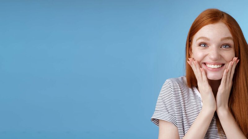 Junge Frau legt lachend die Hända an ihr Kinn